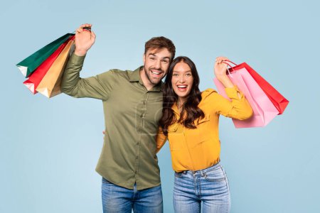 Téléchargez les photos : Rayonnant jeune homme et femme exhibant joyeusement leurs sacs colorés, exsudant bonheur et satisfaction de leur frénésie sur un fond bleu - en image libre de droit