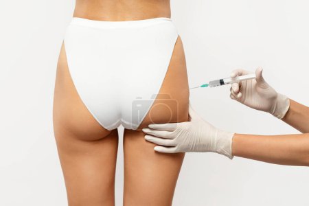 Photo for Close-up of healthcare professional in gloves administering an injection into the upper thigh of european young lady in white underwear. Health and medical anti cellulite treatment - Royalty Free Image