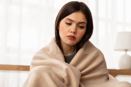 Photo for Upset young frozen woman wrapped with soft beige duvet sits on couch in cold room during turning off home heating in winter season, feeling down, copy space - Royalty Free Image