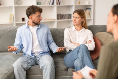 Photo for Millennial couple having quarrel discussing marital problems with counselor at psychologists office, spouses visiting session focusing on resolving issues and restoring harmony in relationship - Royalty Free Image
