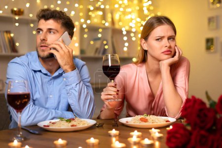 Foto de Durante la cena romántica, la mujer mira con desagrado mientras su acompañante habla por teléfono, creando un momento de desconexión en medio de la luz de las velas - Imagen libre de derechos
