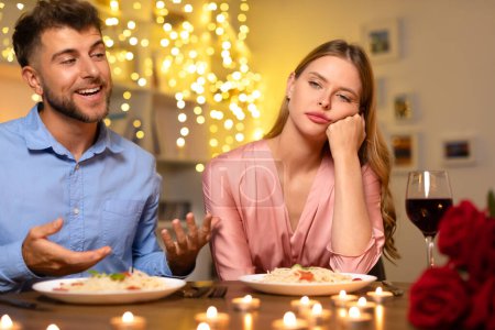 Photo for Disinterested woman rests her cheek on her hand at dinner table, looking away from excited man speaking passionately, highlighting stark contrast in their moods - Royalty Free Image
