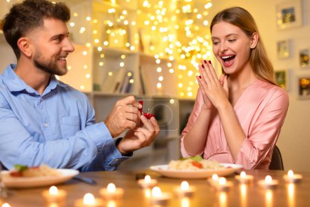 Foto de Mujer encantada se sorprende con el anillo de compromiso chispeante por el hombre sonriente, creando una escena memorable propuesta en una cena romántica a la luz de las velas - Imagen libre de derechos