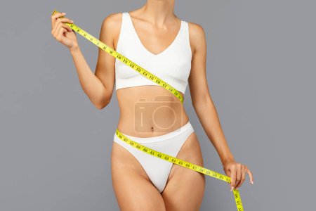 Téléchargez les photos : Jeune femme européenne en vêtements de sport blancs utilisent du ruban à mesurer jaune autour du corps pour mettre en évidence les progrès de remise en forme et la santé, recadrée. Surveillance, résultat de perte de poids, ajustement et sport - en image libre de droit