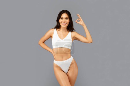 Photo for Glad european slim millennial lady in white underwear with perfect body, show ok sign with hand, isolated on gray studio background. Beauty care recommendation, weight loss, fit ad and offer - Royalty Free Image