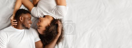 Téléchargez les photos : Au-dessus de la vue d'aimer le couple afro-américain couché au lit ayant moment intime ensemble dans la chambre à coucher à l'intérieur. Les amoureux qui se sourient tendrement. Panorama, Espace Libre - en image libre de droit