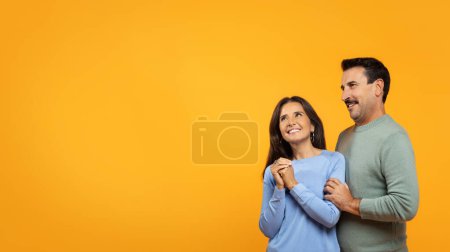 Photo for Happy inspired contented european old woman and man stand close together on orange background, look at distance, suggesting hopeful anticipation. Anticipation and togetherness - Royalty Free Image