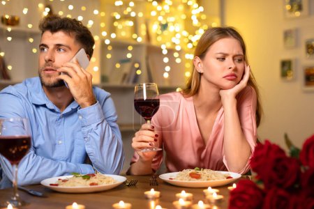 Photo for Man on call ignoring his date, leaving the woman feeling bored and disappointed during a romantic dinner with wine and pasta, atmosphere ruined - Royalty Free Image