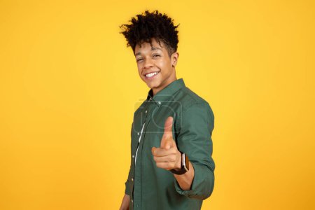 Photo for Stylish cool cheerful young black guy wearing green shirt pointing and smiling at camera, sharing good vibe, posing isolated on yellow studio background, copy space - Royalty Free Image