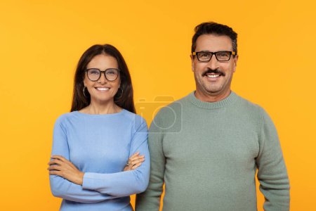 Photo for Happy european old couple in glasses, smiling and confidently standing with arms crossed, project of professionalism and mutual respect on orange backdrop. Professionalism and teamwork - Royalty Free Image