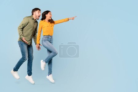 Photo for Joyful man and woman enthusiastically pointing to something off-camera at free space, expressing surprise and delight on a light blue background, banner - Royalty Free Image
