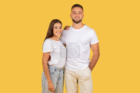 Photo for A smiling caucasian young couple standing close together in casual clothing against a yellow background, radiating happiness and companionship. Love, romantic, date together - Royalty Free Image