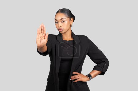 Foto de Serious confident young african american woman in formal suit make stop sign with hand, isolated on gray studio background. Business, work problems, sexism, harassment, issue - Imagen libre de derechos
