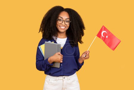 Photo for Joyful black lady student carrying backpack and copybooks holding Chinese flag against yellow background, symbolizing her interest in Chinese language and cultural studies - Royalty Free Image