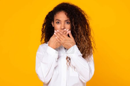 Téléchargez les photos : Millennial black woman covering mouth with hands, isolated on yellow background in studio. Afraid african american lady emotionally reacting to bad news while standing - en image libre de droit