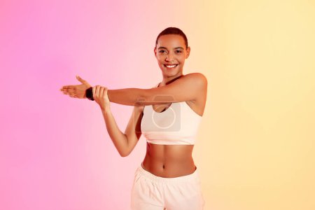 Téléchargez les photos : A smiling woman in sportswear checks her fitness tracker during a workout, showcasing a healthy lifestyle against a gradient pink and yellow backdrop. Fit, sport and health care - en image libre de droit
