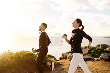Photo for Energetic couple enjoying run along the coast, at sunny day, each carrying water bottles to stay hydrated, highlighting active lifestyle and fitness - Royalty Free Image