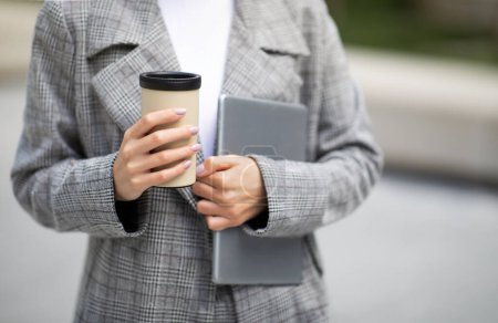 Photo for Cropped Shot Of Young Business Lady Holding Tablet Computer And Paper Coffee Cup Outside. Woman In Jacket Stands With Digital Tab In Urban Area. E-Learning Application, Online Leisure - Royalty Free Image