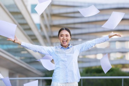 Photo for Happy young asian businesswoman throwing business papers and documents in air, standing outdoors against modern office center building, celebrating freedom. Successful career concept - Royalty Free Image