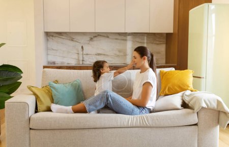 Téléchargez les photos : Young mother and her preschool daughter enjoying playtime on sofa at home, happy mom and cute little female child having fun together in living room, symbolizing loving family bonds, copy space - en image libre de droit