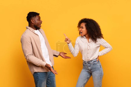 Photo for Angry black man and woman in mid-argument, with expressive gestures and emotions, stand against plain yellow background - Royalty Free Image