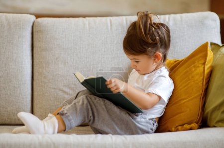 Photo for Cute Little Girl Relaxing On Couch With Interesting Book, Closeup Shot Of Adorable Toddler Female Child Turning Pages, Curious Preschool Kid Expressing Willing To Early Education, Copy Space - Royalty Free Image