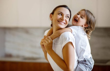 Téléchargez les photos : Laughing child embracing her joyful mother while they playing together at home, happy little girl wrapping her arms around mom, sharing moment of pure joy and connection in a light-filled room - en image libre de droit