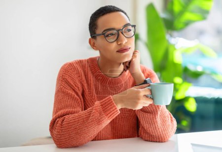 Foto de Pensive millennial latin woman in glasses enjoy lunch and spare time, drink cup of coffee, planning day, think in white cafe, office interior. Break, relax and good morning, create idea, lifestyle - Imagen libre de derechos