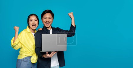 Foto de Overjoyed millennial Asian couple triumphantly raising fists while holding a laptop, signifying success or victory, against a vibrant turquoise blue background, studio - Imagen libre de derechos