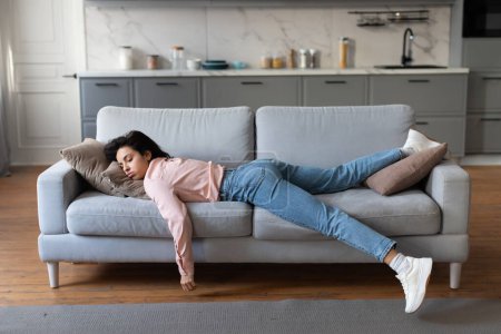 Téléchargez les photos : Woman in pink blouse and jeans lying exhausted on couch, taking well-deserved rest after completing her household cleaning tasks - en image libre de droit
