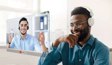 Foto de Black young businessman immersed in virtual video meeting with arabic colleague guy, wearing headphones and looking at digital screen, sitting at modern office. Collage - Imagen libre de derechos