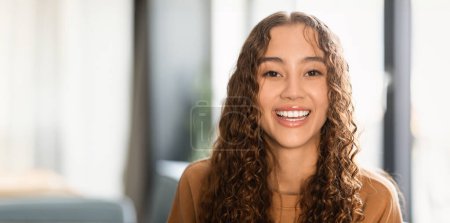 Téléchargez les photos : Portrait of caucasian teenage girl with wavy brown hair indoors, posing confidently looking at camera with carefree and happy expression. Panorama with free space for text - en image libre de droit