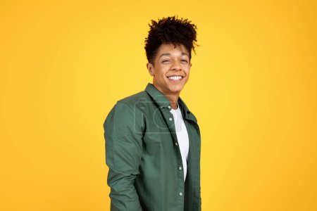 Téléchargez les photos : Portrait of cheerful stylish handsome young african american guy wearing green shirt posing on yellow studio background, smiling at camera, copy space. Millennials lifestyle - en image libre de droit