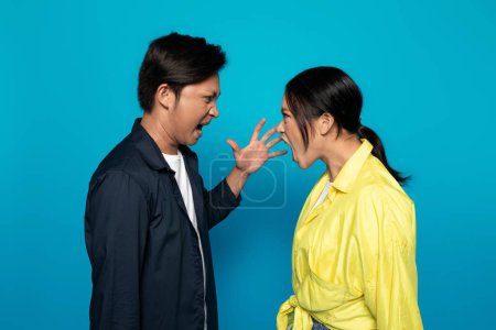 Photo for An Asian millennial man and woman are facing each other with open mouths, as if engaged in a heated argument or shouting match, against a solid turquoise background, studio - Royalty Free Image