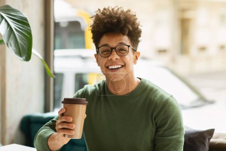Téléchargez les photos : Portrait of happy stylish young black guy wearing eyeglasses enjoying coffee at cafe, holding paper cup and smiling at camera. Millennials lifestyle, leisure concept - en image libre de droit