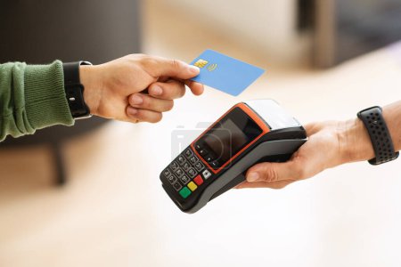 Cropped of man customer paying for goods and services with credit card at cafe or store. Unrecognizable man holding bank card next to wireless payment terminal