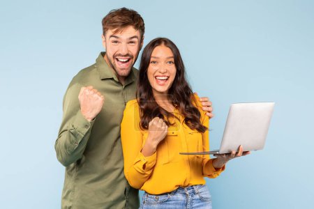 Photo for Overjoyed young couple with laptop celebrating successful moment, both raising their fists in victory, with bright smiles against serene blue background - Royalty Free Image