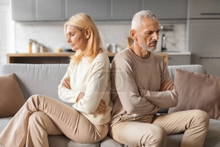 Téléchargez les photos : Upset senior married couple grey-haired man and blonde woman sit back to back on couch at home, not talk to each other, feeling down after fight, have difficulties in marriage, thinking about divorce - en image libre de droit