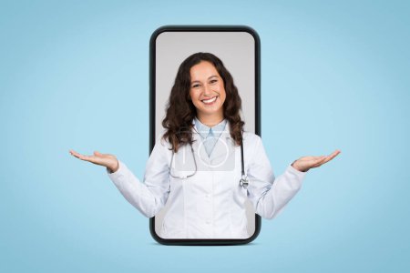 Téléchargez les photos : Digital healthcare concept with smiling female doctor displayed inside smartphone frame, hands raised in balancing gesture on blue background - en image libre de droit