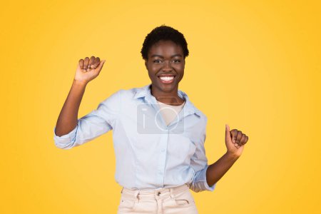 Foto de Glad teen african american lady student, exuding triumph and joy, dance, enjoy music, isolated on yellow background, studio. Celebrate success and win, fun and spare time - Imagen libre de derechos