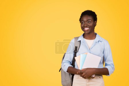 Téléchargez les photos : A focused black woman student, immersed in studies with pile of books, expression serious and studious, striking yellow background, epitomizing essence of academic dedication and learning - en image libre de droit