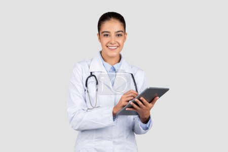 Téléchargez les photos : Une femme médecin européenne joyeuse avec un stéthoscope tient une tablette numérique, incarnant l'intersection de la médecine traditionnelle et de la technologie moderne dans les soins de santé, la publicité et l'offre - en image libre de droit