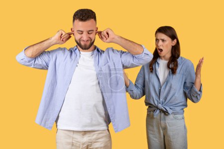 Foto de Hombre con los oídos cubiertos ignora a la mujer que parece estar discutiendo o expresando frustración, que representa la ruptura de la comunicación en el fondo amarillo - Imagen libre de derechos