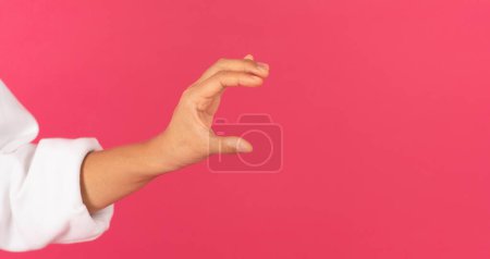 Téléchargez les photos : Main féminine tenant un objet invisible sur fond rose, femme méconnaissable annonçant quelque chose, montrant un endroit pour se maquiller, debout isolé sur un fond lumineux, plan recadré, panorama - en image libre de droit