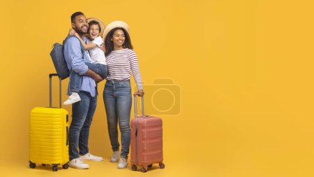 Téléchargez les photos : Offre de voyage. Heureuse belle famille noire avec des valises regardant à côté de l'espace de copie, joyeux jeunes parents afro-américains et petit fils embrassant et souriant, debout sur fond jaune - en image libre de droit