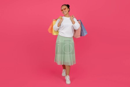 Photo for Happy Asian Woman Walking With Bright Shopping Bags In Hands On Pink Background, Joyful Smiling Female Carrying Purchases And Looking At Camera, Enjoying Black Friday Sales, Full Length, Copy Space - Royalty Free Image