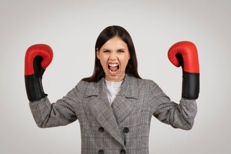 Photo for Fierce young businesswoman in plaid blazer, wearing boxing gloves and showing fighting spirit, metaphorically prepared for a challenging task - Royalty Free Image
