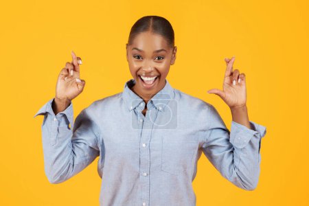 Photo for Joyful black woman crossing fingers making wish, hopes for fortune and good luck, posing against yellow background, portrait of lady making cherished wishes while smiling to camera - Royalty Free Image