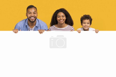 Photo for Offer for families. African american parents and little son leaning on blank white advertisement board with free space, happy black mother, father and male kid demonstrating template for ad, mockup - Royalty Free Image