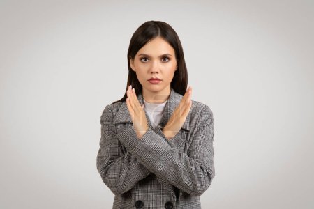 Photo for Determined young woman in houndstooth blazer makes negative no gesture, crossing her hands in front with a serious expression on a plain background - Royalty Free Image